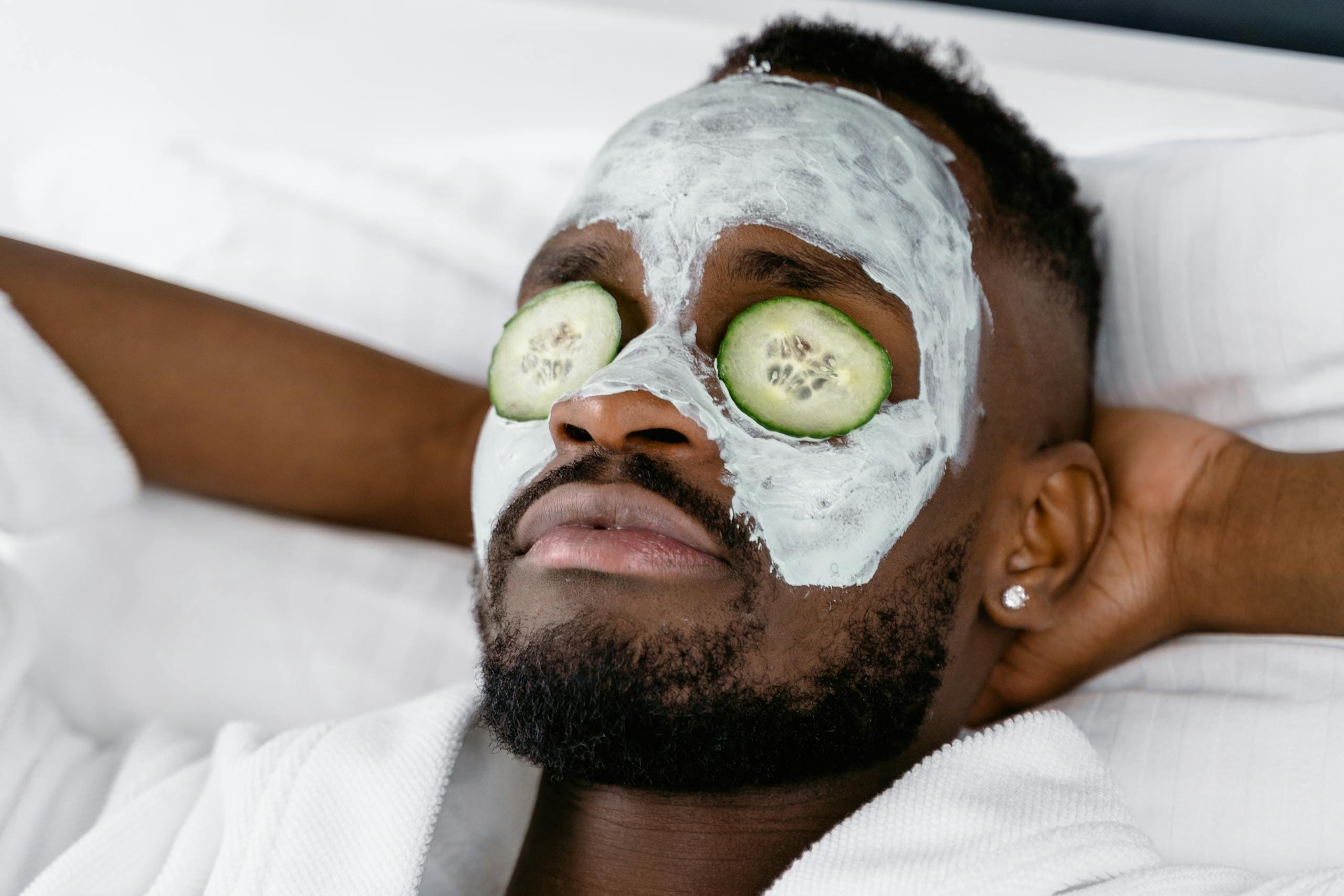 A man enjoying a self-care day with a face mask and cucumber slices for relaxation.